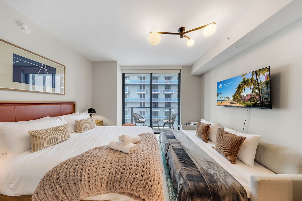 Une chambre d’hôtel moderne dotée d’un grand lit, d’un canapé, d’une télévision et d’un balcon offrant une vue sur la ville.