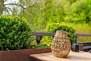 Un vase en osier posé sur un banc en bois, avec de la verdure et des fleurs en arrière-plan.
