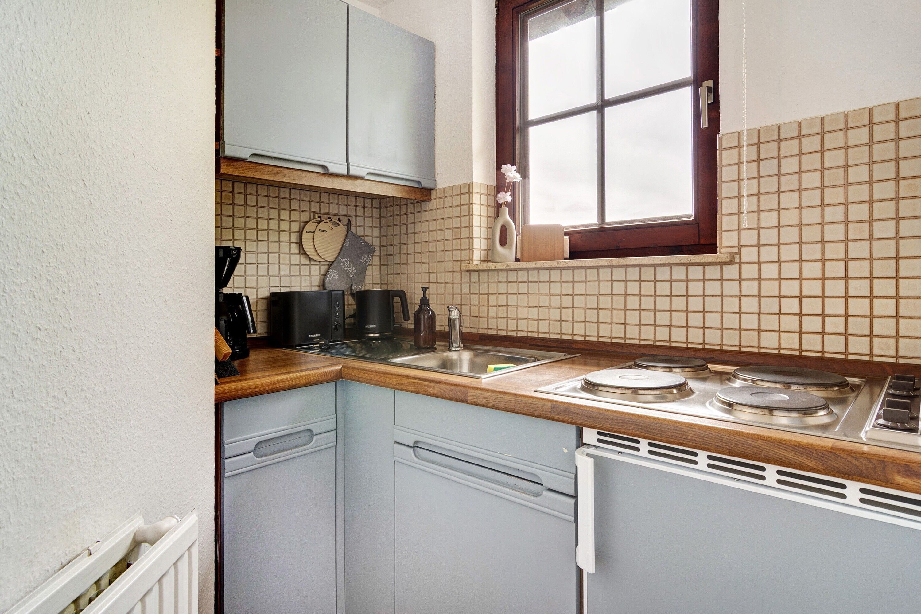 Una cocina compacta con lavavajillas, estufa y ventana sobre el fregadero.
