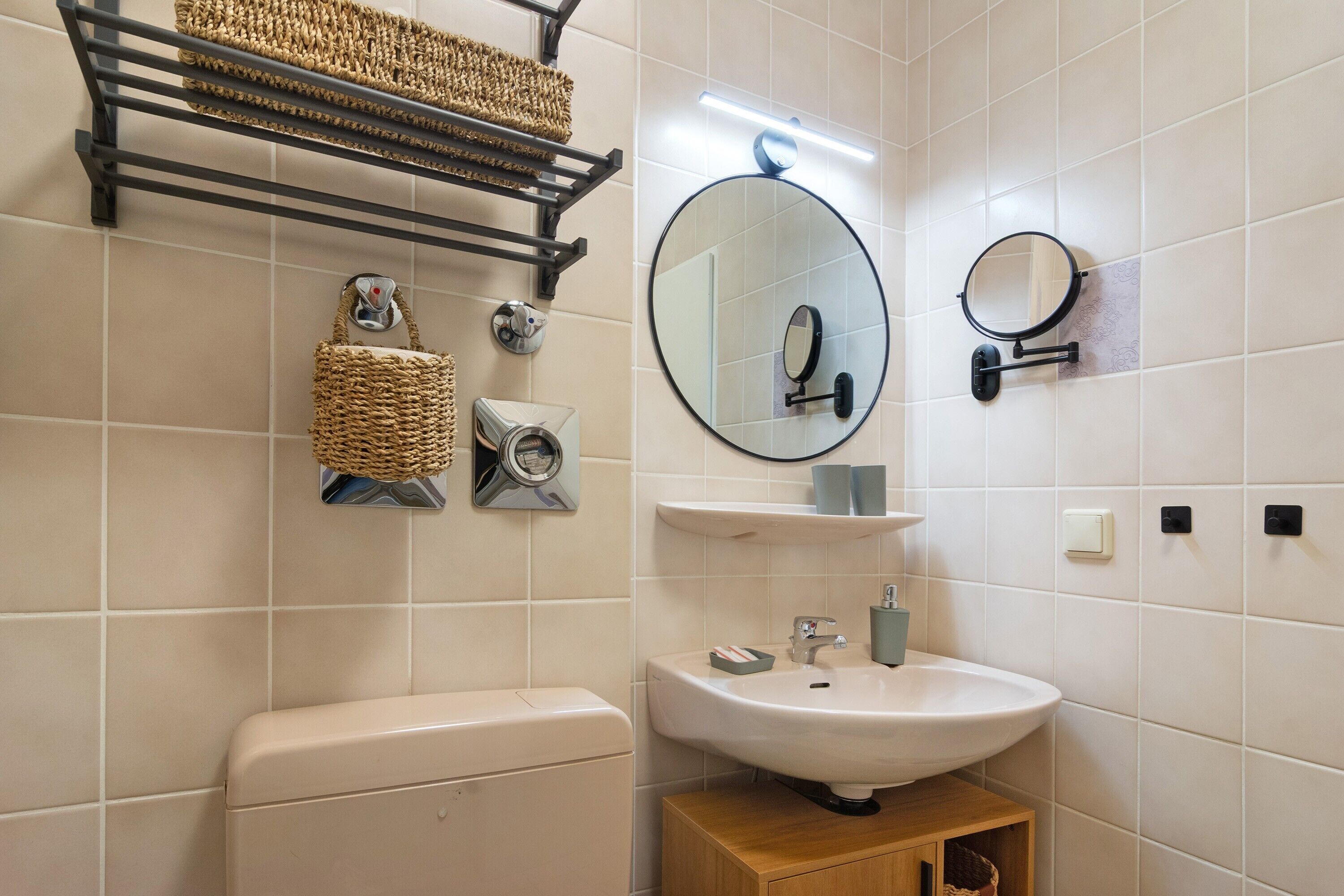 A bathroom with a toilet, sink, mirror, towel rack, and a small wooden cabinet.