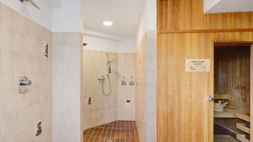 Zona de ducha con paredes de azulejos, una puerta de madera y un cartel que indica una sauna.