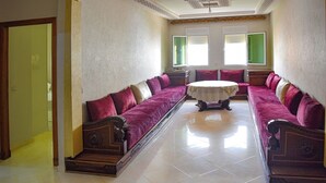 A spacious room with a long sofa, a round table, and a door leading to another area. - Dream apartment tanger (Tanger)