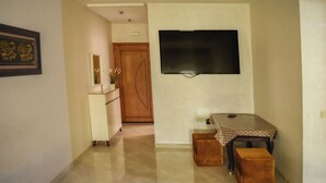 A hallway with a TV mounted on the wall, a small table with a patterned tablecloth, and a brown ottoman. - Dream apartment tanger (Tanger)
