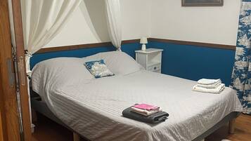 A bedroom with a bed, a bedside table, a lamp, a nightstand, a window with curtains, and a painting on the wall.