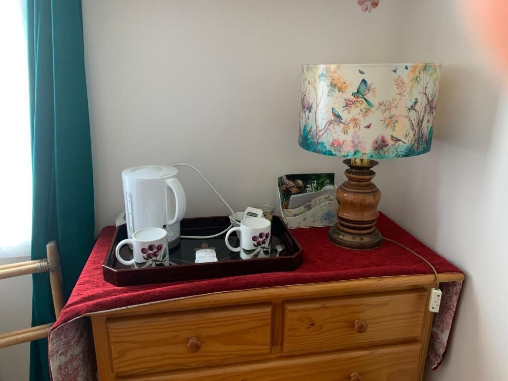 A wooden dresser with a red cloth, a white coffee maker, a white mug, a tray, and a lamp with a floral design.
