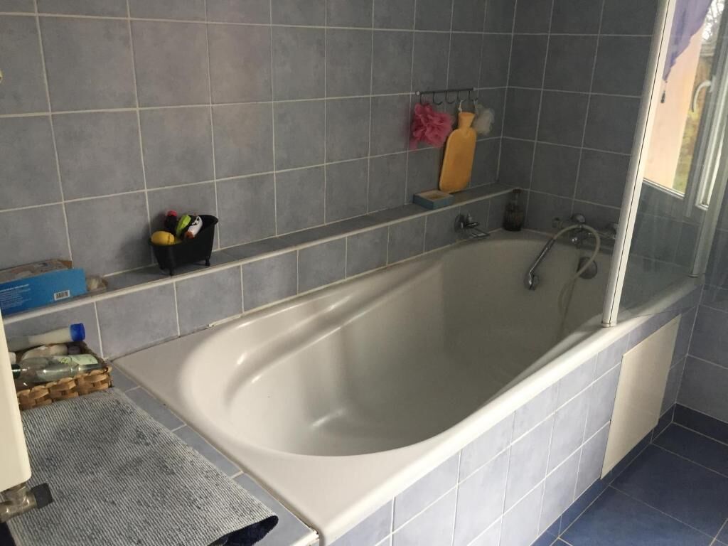 Een badkamer met een bad, een handdoekhouder met een roze handdoek, en een plank met toiletartikelen.
