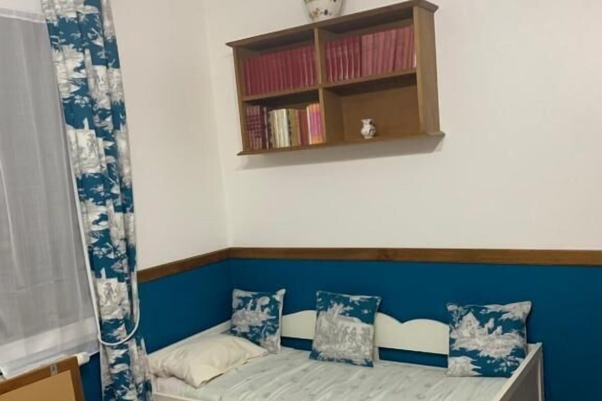 A bedroom with a bed, a bookshelf, a window with a curtain, and a wall-mounted vase.