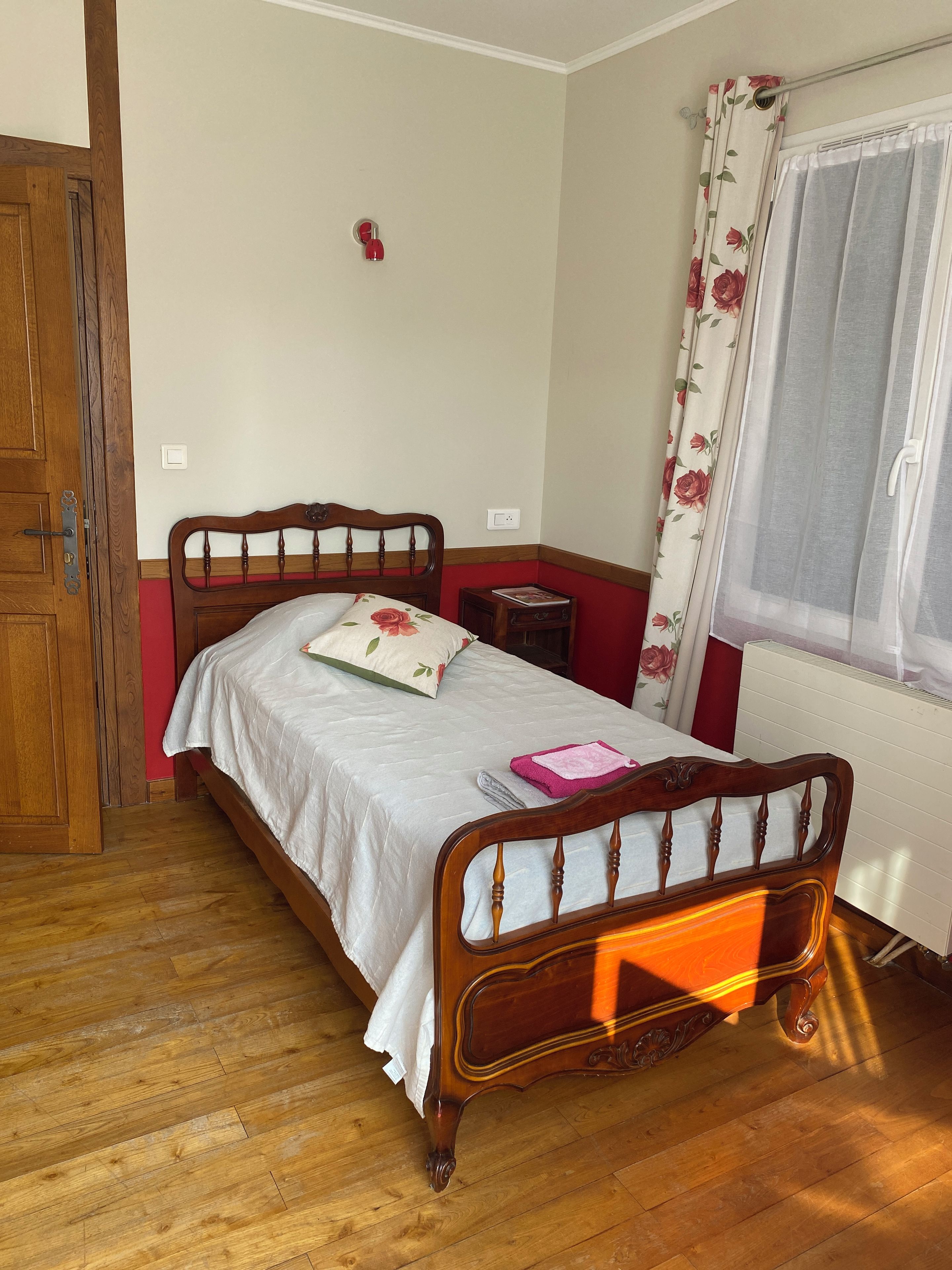 A bedroom with a wooden bed, a bedside table, a radiator, and a window with curtains.