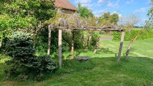 Un jardin agrémenté d’une pergola en bois, d’un sentier en pierre et d’une maison en arrière-plan.