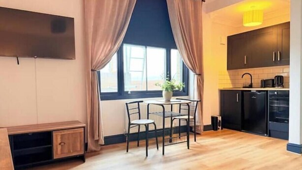 Una cocina moderna con armarios negros, un comedor con una mesita y sillas, y un ventanal con cortinas.