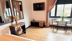 Una habitación con cama, escritorio, silla, televisor y ventana con cortinas.