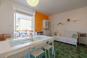Ein Zimmer mit Esstisch, Stühlen, einer Couch, einem Schrank und einem kleinen Regal mit Gegenständen.