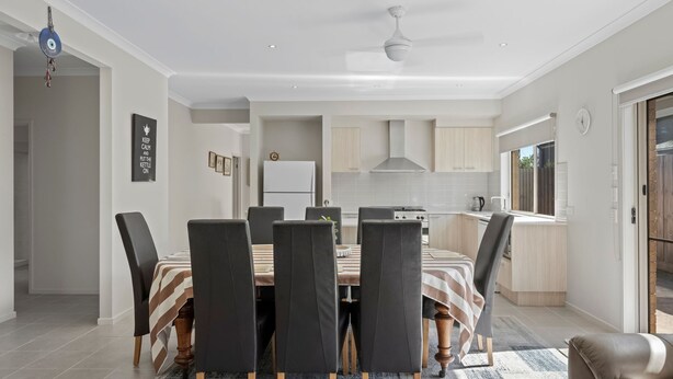 Un comedor moderno con una mesa y sillas, una cocina al fondo y vistas por una ventana.