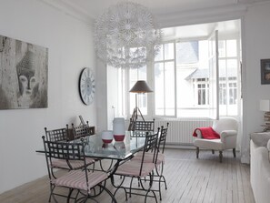 Un coin repas avec une table en verre, des chaises en métal, une grande horloge murale et un luminaire décoratif au plafond.