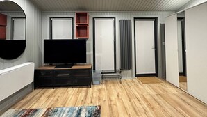 Egy modern nappali, melyben síkképernyős televízió, parketta, egy nagy tükör és beépített polcrendszer található.