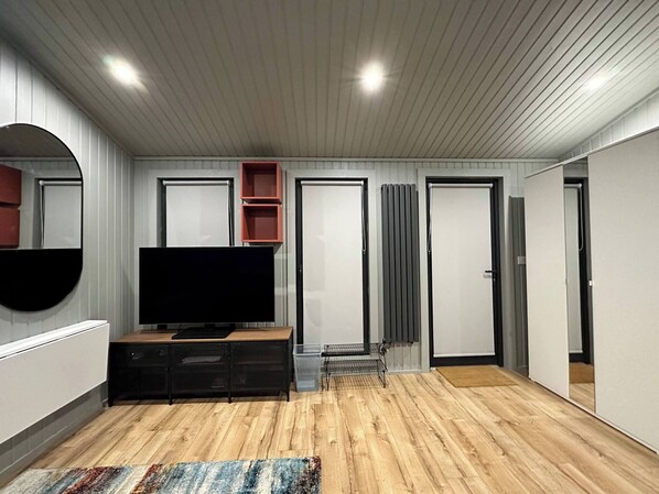 A modern living room with a flat-screen TV, wooden flooring, a large mirror, and built-in shelving. - A Fully Private Studio in Dublin Made for You! (Lucan)