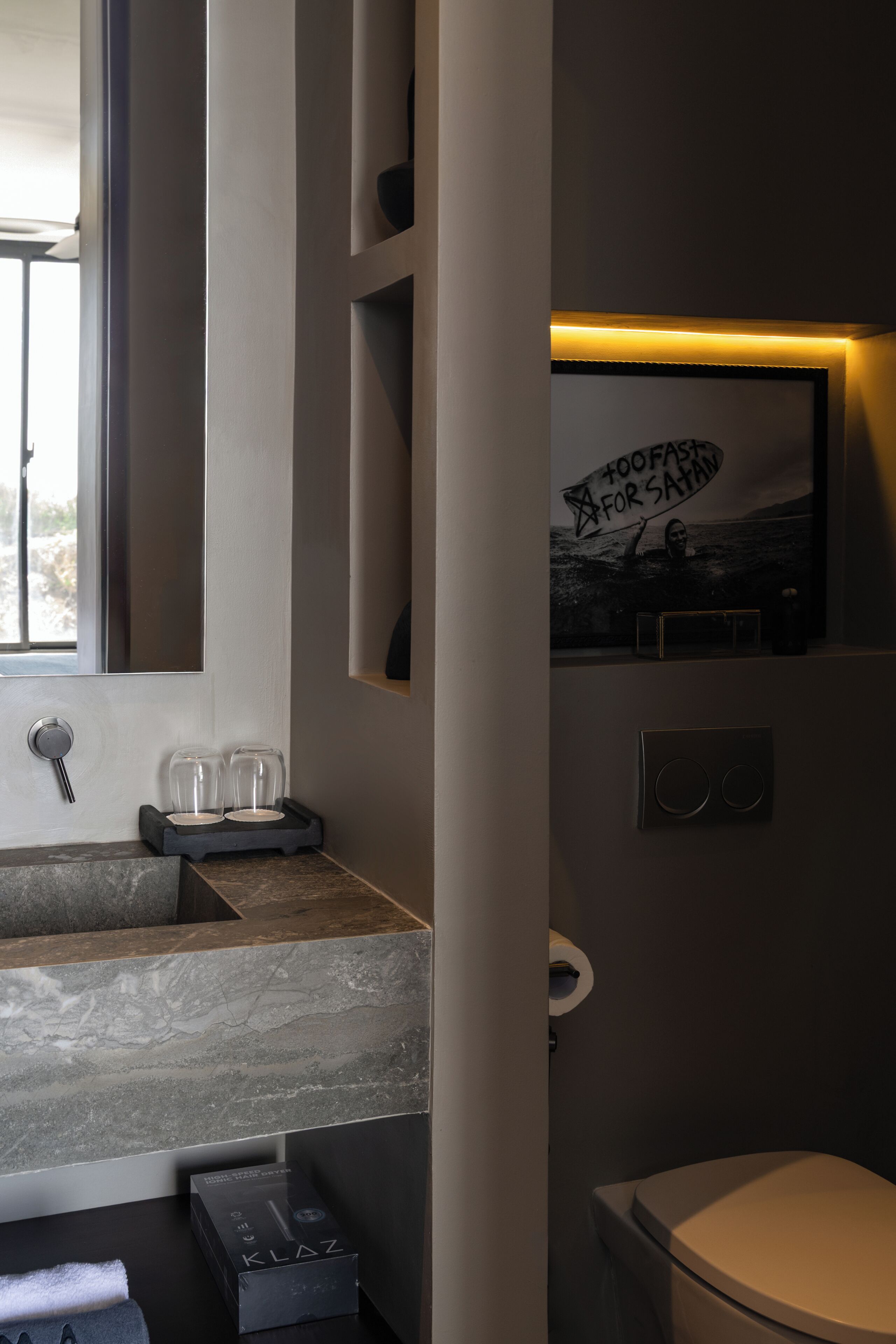 A modern bathroom with a marble sink, a toilet, a framed poster, and a towel rack.
