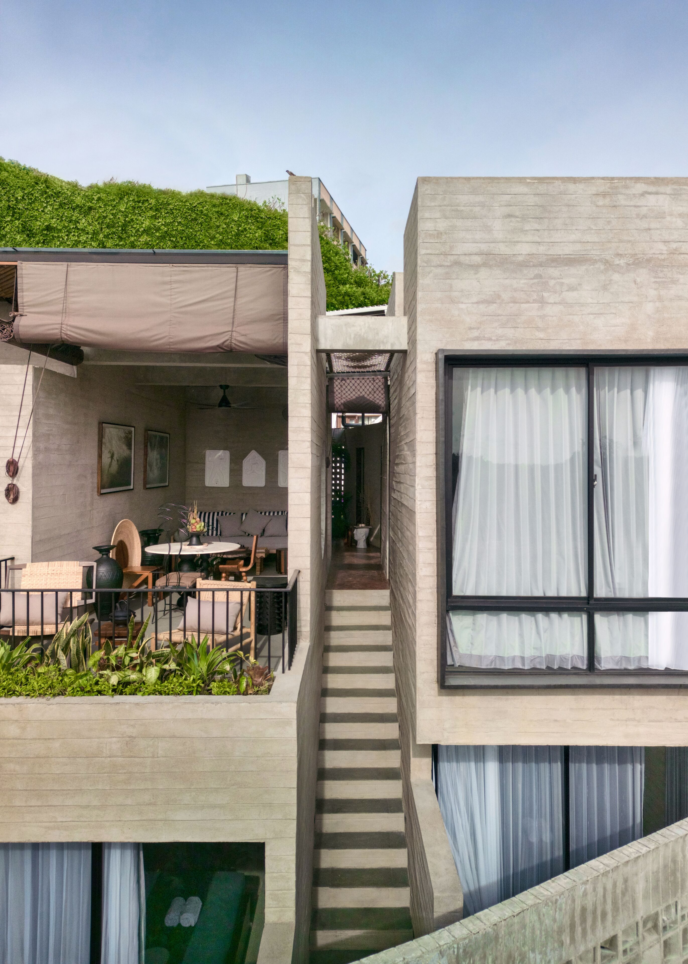 A modern building with a flat roof garden, a staircase leading to an upper level, and a dining area with outdoor furniture.