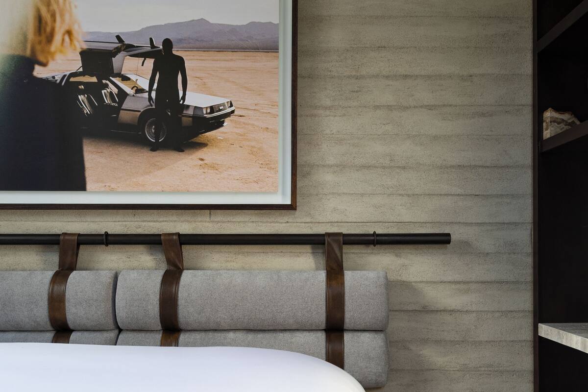 Ein Bett mit Kopfteil, ein gerahmtes Bild von einer Wüstenlandschaft und ein Holzregal.