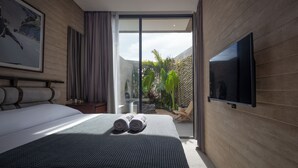 Quarto de hotel moderno com uma cama grande, televisão de tela plana e vista para um jardim.