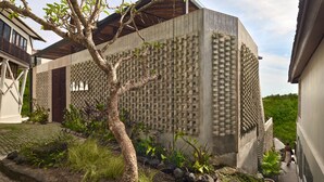 A modern building with a unique brick pattern facade, a tree in the foreground, and a paved pathway. - Orama Bali (Pecatu)