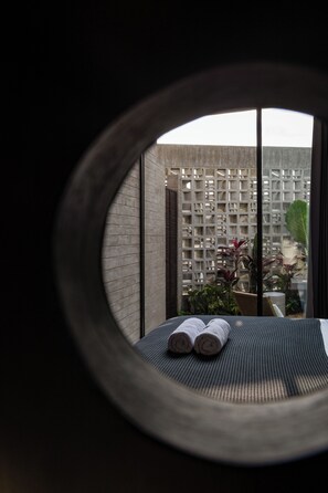 A circular window view of a room with a bed, a woven mat, and a plant. - Orama Bali (Pecatu)