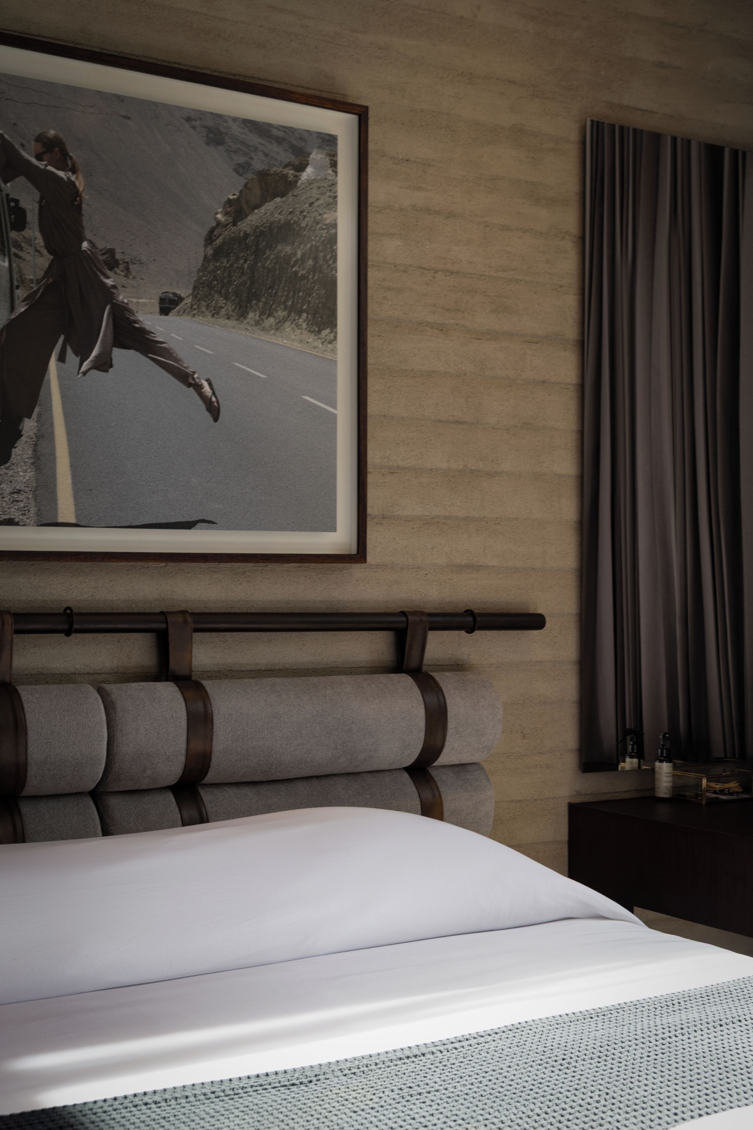 A hotel room with a bed, a framed picture on the wall, a window with curtains, and a bedside table.