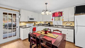 Une cuisine avec des meubles blancs, un four à micro-ondes, une cuisinière, un évier et une table à manger avec des chaises.