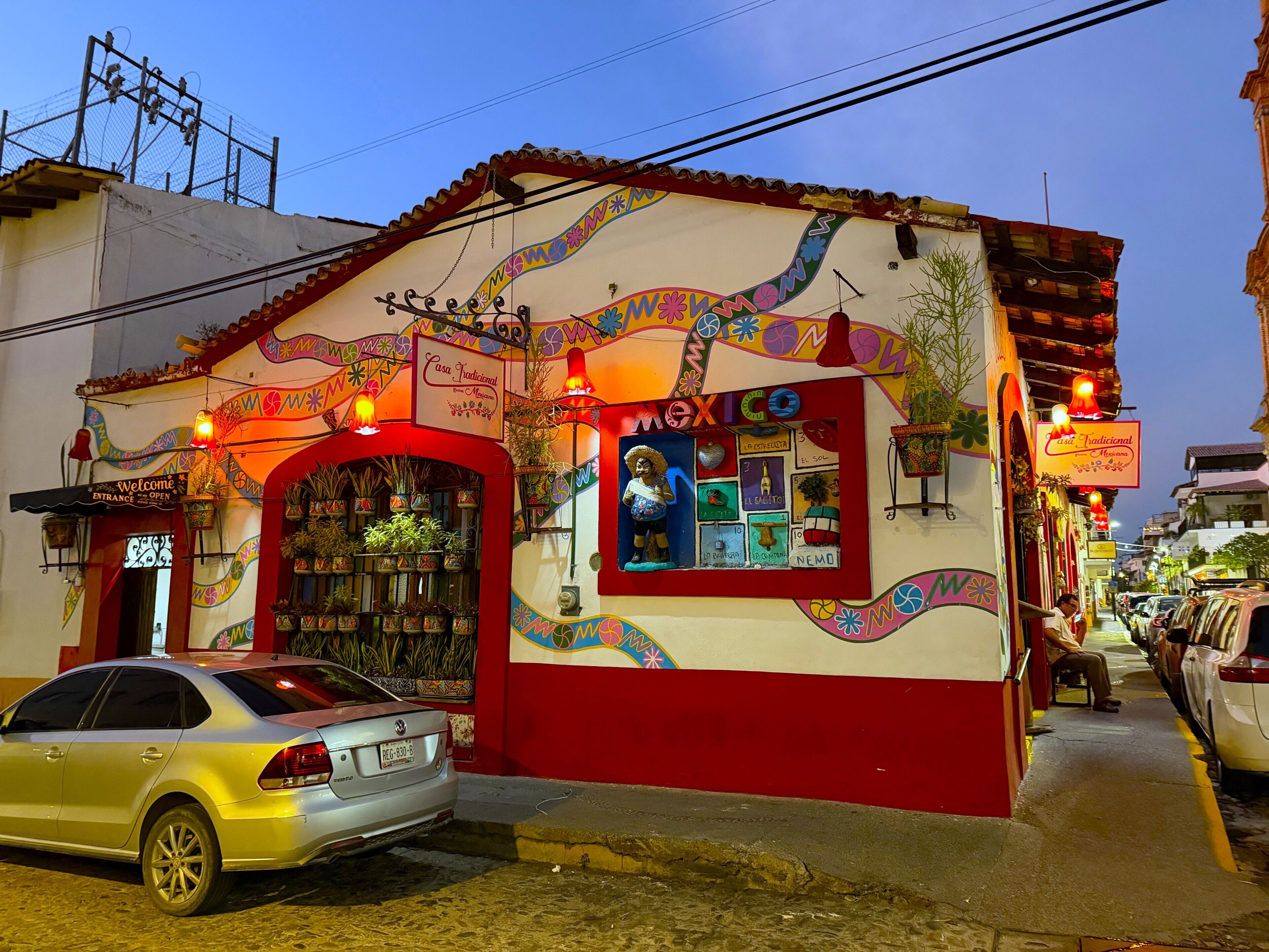 A building with a colorful mural, a sign reading 'Casa Traditional Mexicana,' and a parked car in front.