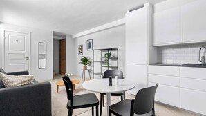 Een moderne keuken met witte kasten, een ronde eettafel met stoelen, en een bank in de woonkamer.
