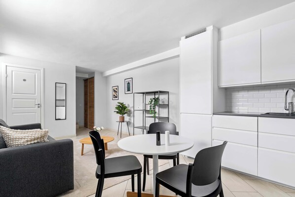 A modern kitchen with white cabinets, a round dining table with chairs, and a sofa in the living area.