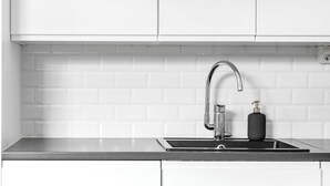Een keuken met witte kastjes, een roestvrijstalen spoelbak en een zwarte zeepdispenser.