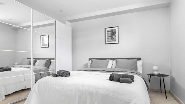 Een moderne slaapkamer met een groot bed, een nachtkastje, een spiegel en een lijst met een afbeelding aan de muur.