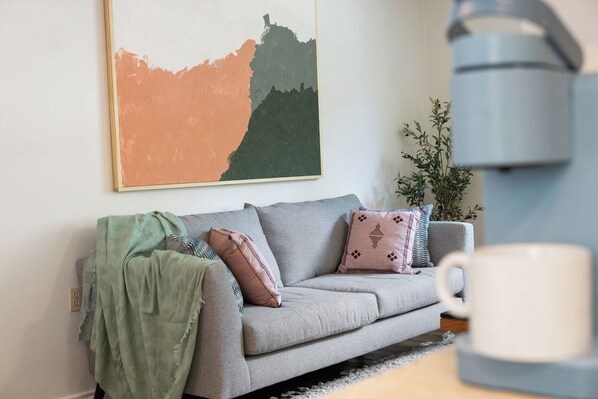 A living room with a grey sofa, a green throw blanket, and a white mug on a table.
