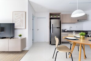 A modern kitchen with a built-in refrigerator, a dining table with chairs, and a television on a cabinet. - Cannes Breeze By The Sea 1Bed with Sofa bed / Pool / Gym / Patio / Barbecue (Florianópolis)