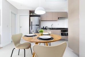 Uma cozinha moderna com área de refeições, incluindo uma mesa de madeira redonda, duas cadeiras, uma luminária pendente e uma geladeira.