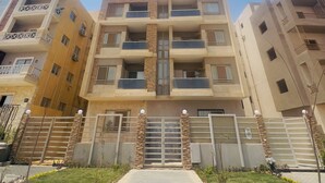 Un edificio residencial de varios pisos con balcones, entrada protegida por un portón y camino de acceso pavimentado.
