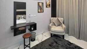 Un dormitorio moderno con cama, tocador con espejo, una silla y un amplio ventanal con cortinas.