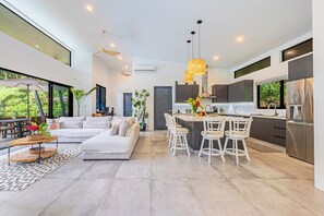Una cocina moderna con una isla central, taburetes blancos y una zona de comedor.