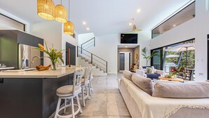 A modern kitchen with a central island, a dining area with chairs, a sofa, and a TV mounted on the wall. - Stunning 4-bedroom villa with infinity pool, 15 min. from Dominical (Uvita)
