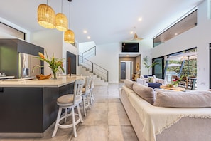 A modern kitchen with a central island, a dining area with chairs, a sofa, and a TV mounted on the wall. - Stunning 4-bedroom villa with infinity pool, 15 min. from Dominical (Uvita)