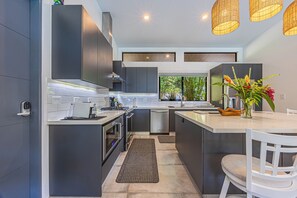 Une cuisine moderne avec des meubles de couleur sombre, un îlot central, un four encastré et une fenêtre donnant sur un espace verdoyant.