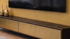 A flat-screen TV mounted on a wall above a long, dark-colored console with multiple drawers. - Four Seasons - Carnival Summer Lounge (Aalborg)