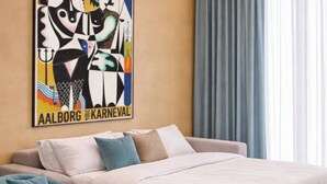 A bedroom with a bed, a blue armchair, a large abstract painting, and a window with curtains. - Four Seasons - Carnival Summer Lounge (Aalborg)
