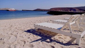 Una playa con sillas de playa blancas, un bote en el agua y colinas al fondo.