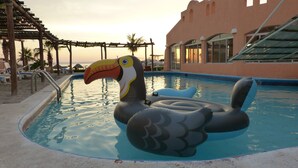 Una piscina con juguetes inflables, una pérgola y un edificio con ventanas arqueadas.