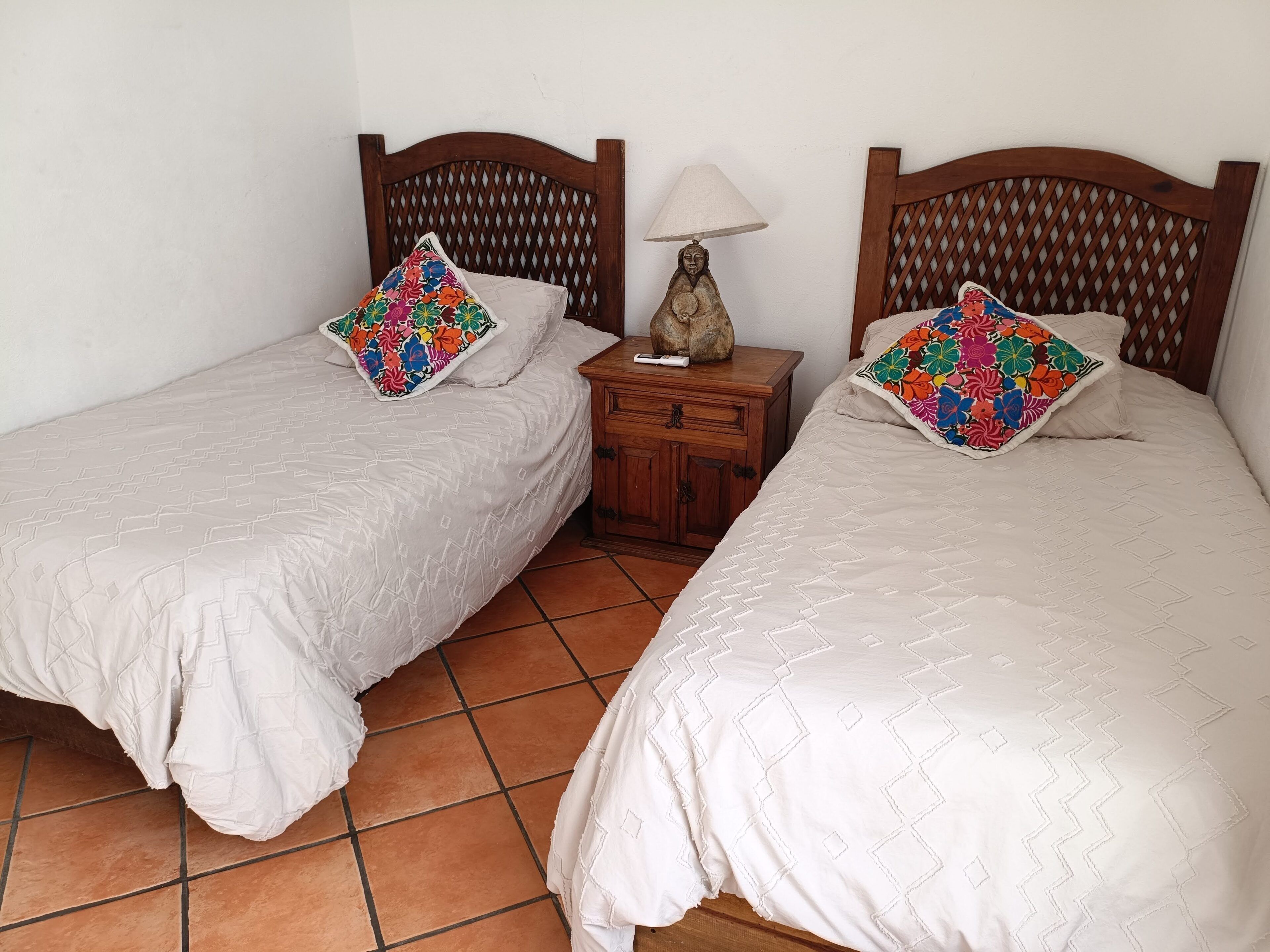 Two single beds with wooden headboards, a nightstand with a lamp, and a tiled floor.