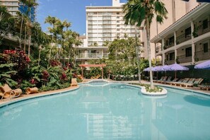 Una piscina rodeada de sillones de descanso y sombrillas, con un edificio de hotel al fondo.