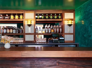 Zona de bar con estantes de botellas de licores, una caja registradora y un florero con flores en la barra.