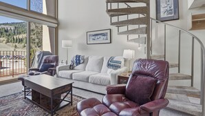 Ein geräumiger Wohnbereich mit Sofa, Ledersessel, Couchtisch und einer Treppe.